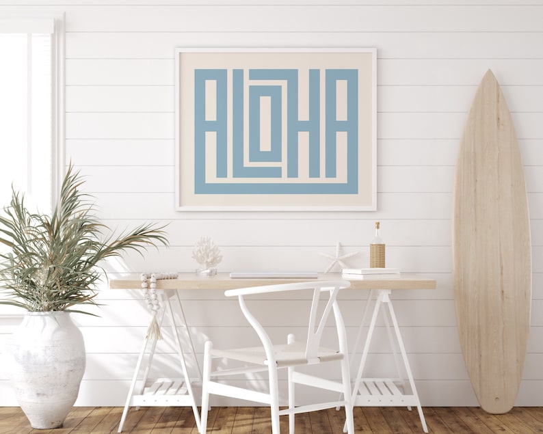 K&ouml;nnte beinhalten: Ein gerahmter Druck mit einem hellblauen geometrischen Design des Wortes "ALOHA" auf cremefarbenem Hintergrund. Der Druck h&auml;ngt an einer wei&szlig;en Schiffslappenwand &uuml;ber einem wei&szlig;en Schreibtisch mit einem wei&szlig;en Stuhl und einem Surfboard aus Holz.