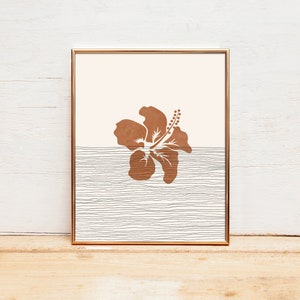 May include: A framed print featuring a brown hibiscus flower silhouette against a light pink background. The lower half of the print displays a white and grey striped pattern.