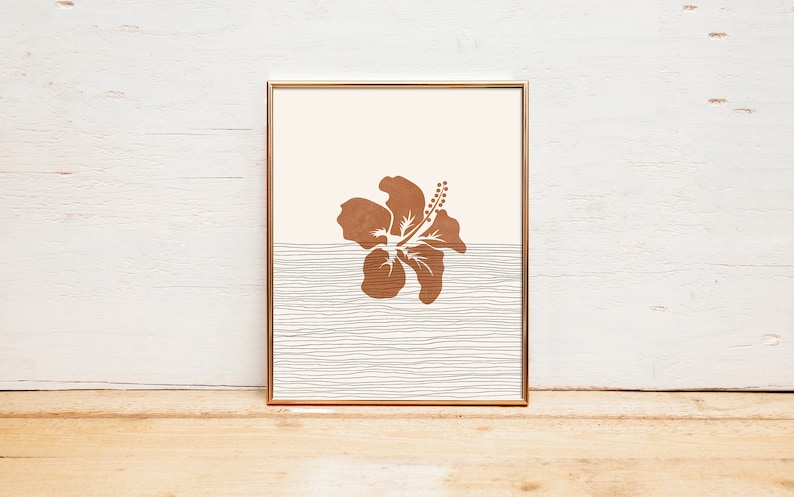 May include: A framed print featuring a brown hibiscus flower silhouette against a light pink background. The lower half of the print displays a white and grey striped pattern.