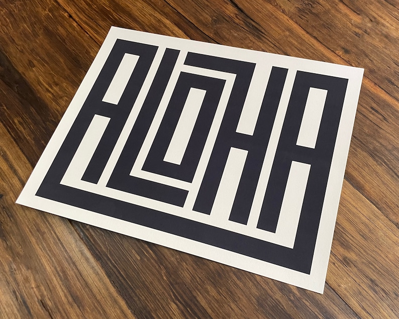 K&ouml;nnte beinhalten: Eine wei&szlig;e Karte mit dem Wort "ALOHA" in schwarzer Schrift, in einem geometrischen Design.