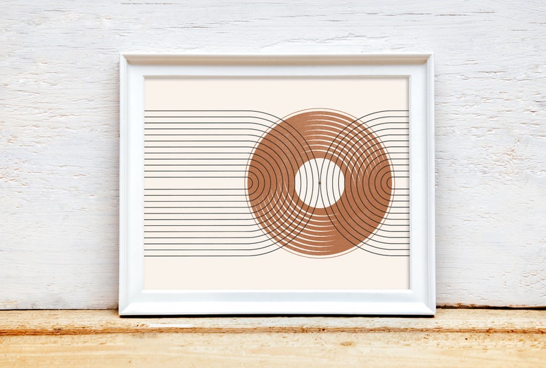 May include: A framed print with a minimalist geometric design. The print features a brown circle with concentric rings, intersected by black lines.