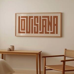 Puede incluir: Una impresi&oacute;n enmarcada con la palabra "LOUISIANA" en una fuente geom&eacute;trica marr&oacute;n sobre un fondo blanco.