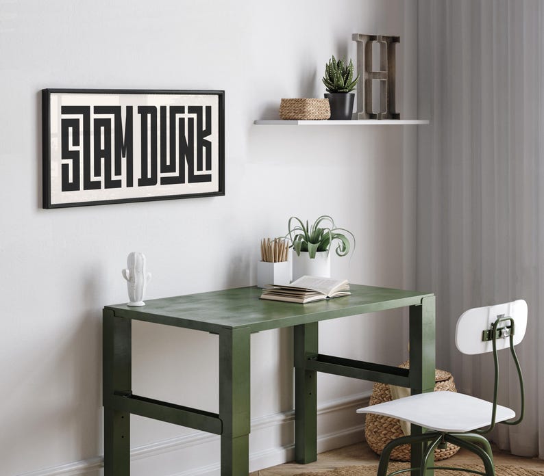 May include: A black framed print with the word "SLAM DUNK" in white letters. The print is hanging on a white wall above a green metal desk with a white chair. There are plants and a wooden shelf with a wooden letter H on the wall.