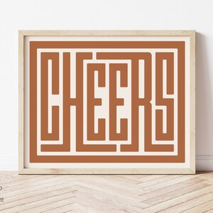 May include: A framed print with a brown background and the word "CHEERS" in a stylised font.