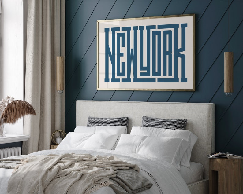 May include: A white bed with a beige blanket and white pillows in a bedroom with a blue wall and a gold framed print that says "NEW YORK" in blue letters.