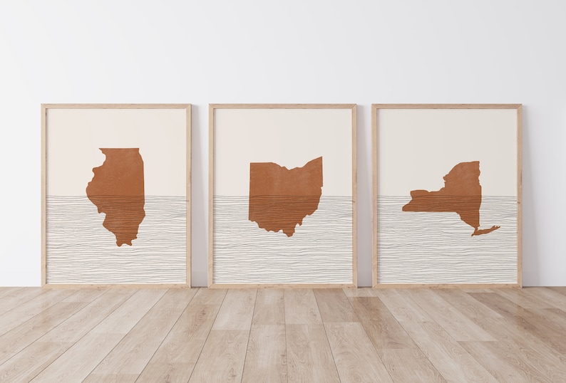 May include: Three framed prints featuring the outlines of the states of Illinois, Ohio, and New York. Each state is depicted in a burnt orange color against a white background with a subtle textured pattern of horizontal lines.