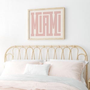 K&ouml;nnte beinhalten: Ein gerahmter Druck mit dem Wort "MIAMI" in rosa Buchstaben auf wei&szlig;em Hintergrund. Der Druck h&auml;ngt an einer wei&szlig;en Wand &uuml;ber einem hellbraunen Korbkopfteil.