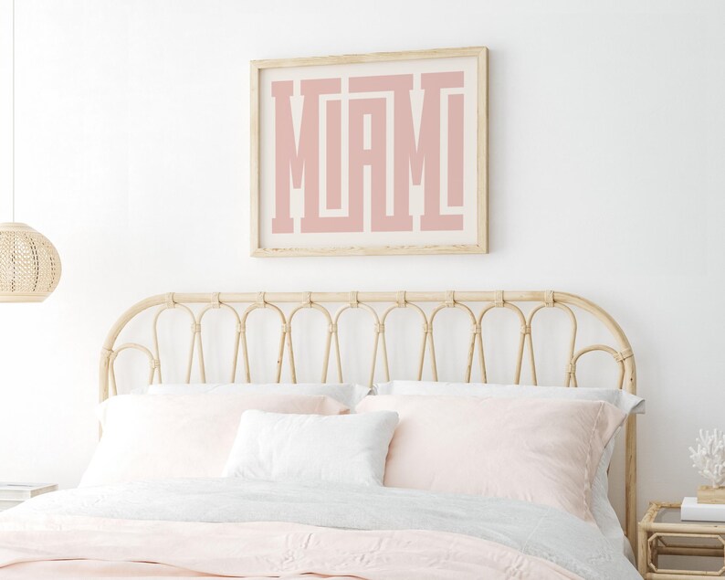 K&ouml;nnte beinhalten: Ein gerahmter Druck mit dem Wort "MIAMI" in rosa Buchstaben auf wei&szlig;em Hintergrund. Der Druck h&auml;ngt an einer wei&szlig;en Wand &uuml;ber einem hellbraunen Korbkopfteil.
