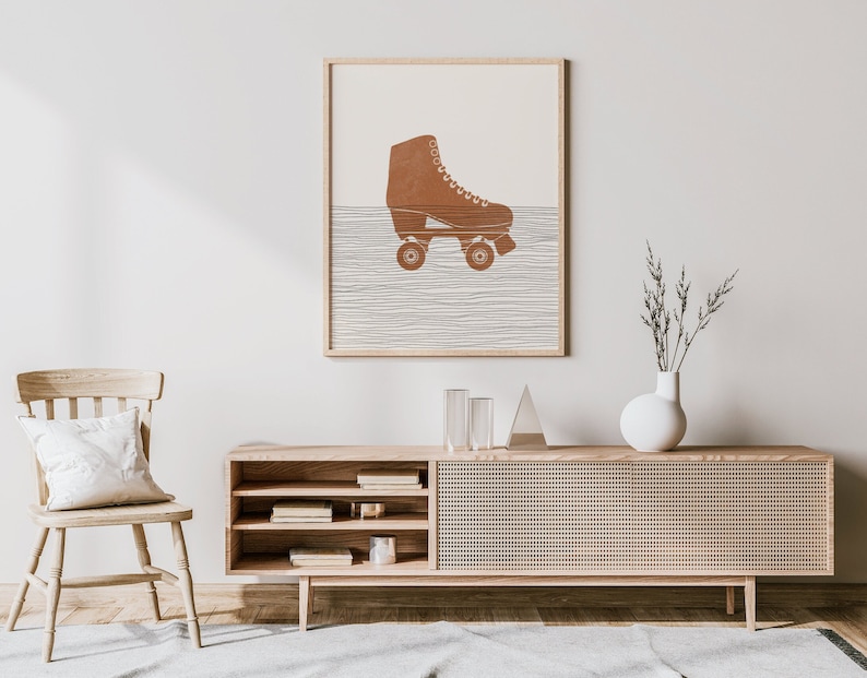 Op de afbeelding: Een ingelijste print van een bruine rolsschaats op een witte achtergrond met een patroon van dunne grijze lijnen. De rolsschaats staat op een lichtbruin houten frame.