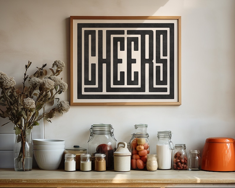 May include: A framed black and white print with the word "CHEERS" in a geometric design. The print is hanging on a white wall above a countertop with various glass jars and bowls.