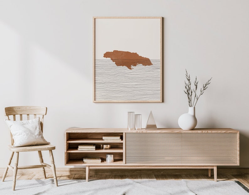 Puede incluir: Un interior de sala de estar minimalista con una consola multimedia de madera, una silla blanca y una impresi&oacute;n enmarcada de una isla marr&oacute;n con l&iacute;neas blancas sobre un fondo beige.