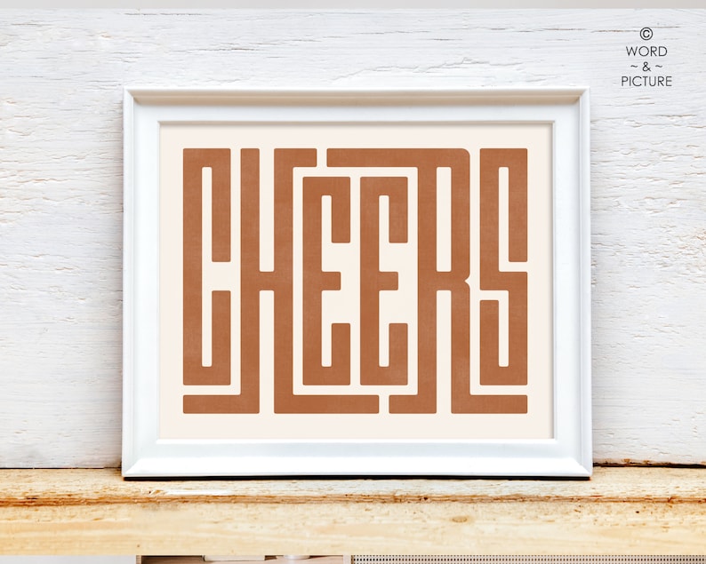 May include: A white framed print with the word "CHEERS" in a brown, geometric font on a cream background.