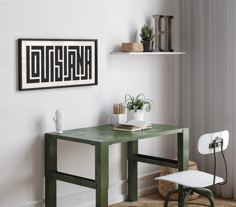 Puede incluir: Una impresi&oacute;n enmarcada en blanco y negro con la palabra "LOUISIANA" en un dise&ntilde;o geom&eacute;trico. La impresi&oacute;n est&aacute; colgada en una pared blanca sobre un escritorio de metal verde con una silla blanca. Hay plantas y un estante con una letra H de madera en la pared.