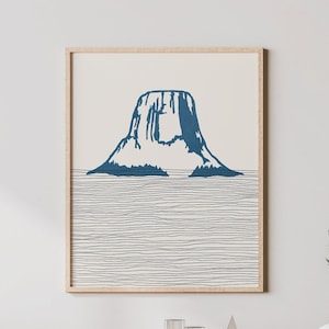 May include: A framed print of a blue mountain silhouette against a white background. The mountain is surrounded by thin black lines that resemble water.