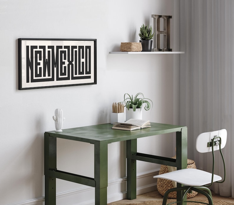 May include: A framed black and white print of "NEW MEXICO" in a geometric design hangs above a green desk. A white cactus figurine sits on the desk. A white shelf holds a plant and decorative items.