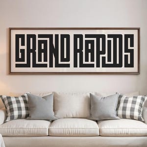 May include: A white sofa with black and white checked throw cushions and a grey throw cushion. A framed print with the text "GRAND RAPIDS" in black letters is hanging on the wall behind the sofa.