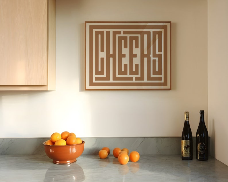 May include: A kitchen counter with a brown bowl filled with oranges, two bottles of wine, and a framed print with the word "CHEERS" in a brown geometric design.