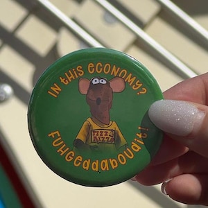 May include: A round green pinback button featuring a brown rat character wearing a yellow t-shirt with the text Pizza Rizzo. The text In this economy? is printed in orange at the top, and the text Fuhgeddaboudit! is printed in orange at the bottom.