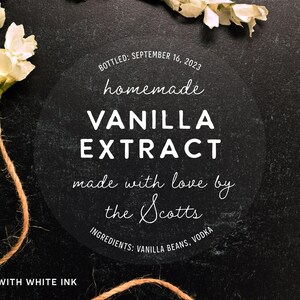 May include: A clear, round label with white text reading "homemade VANILLA EXTRACT" with the text "made with love by the Scotts." The label also includes the bottling date and ingredients. The label is surrounded by white flowers and twine.
