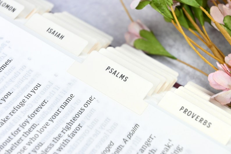 May include: Close-up of a white book with tabs labeled "Solomon", "Isaiah", "Psalms", and "Proverbs".