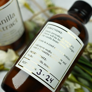 Puede incluir: Dos botellas de vidrio marr&oacute;n de extracto de vainilla con etiquetas doradas. Las etiquetas incluyen el texto "Extracto de vainilla", "Instrucciones" e "Ingredientes: Vodka y vainas de vainilla". Una botella est&aacute; etiquetada "Embotellado el: 3.24".