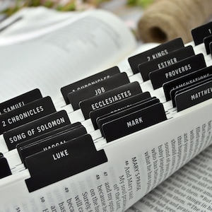 May include: Close-up of a black and white Bible with black tabs marking each book of the Bible. The tabs are labeled with the names of the books, including "Song of Solomon", "Mark", "Matthew", "Esther", "Proverbs", and "1 Kings".