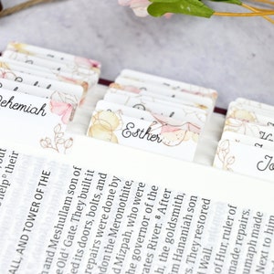 May include: Close-up of a Bible with colorful floral bookmarks for the books of Nehemiah, Esther, and Job. The bookmarks are made of paper and have a watercolor design.