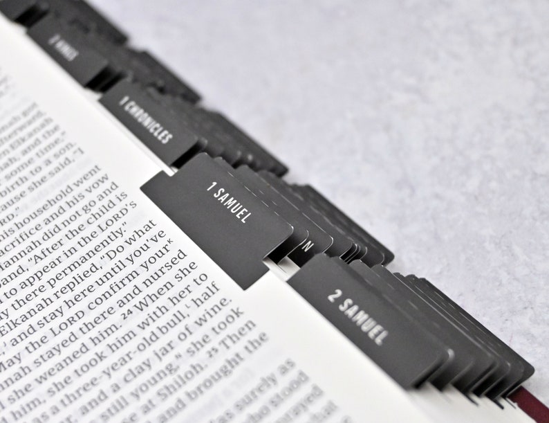 May include: Close-up of a Bible with black tabs marking the books of 1 Chronicles, 1 Samuel, and 2 Samuel. The tabs are arranged in a row, with the tab for 1 Samuel in the center.