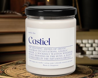 May include: A white candle with a black lid and label. The label reads "smells like Castiel" and includes the text "THE AROUSING AROMA OF EROTIC ENOCHIAN INCANTATIONS, ANGELIC ARDOR. A WICKEDLY WANTON WINGSPAN WUNKY HEROISM ON THE HUNT. & ILLICIT INTERLUDES IN THE INFAMOUS IMPALA 100% vegan soy candle | cotton wick | ethically sourced and made Haute & Dangerous".