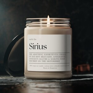 Puede incluir: Una vela beige en un tarro de vidrio con una tapa negra. La vela est&aacute; encendida y la etiqueta dice "smells like Sirius" y "THE AROUSING AMORTENTIA AROMA OF BAD BOY BRAVADO, ANIMALISTIC ANIMAGUS ALLURE & MAKING SOME MISCHIEF ON THE MOTORBIKE".