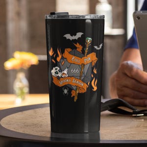 May include: Black travel tumbler with a Halloween-themed design. The tumbler features a D20 die with the number 666, flames, bats, a skull, and the text "Roll for Spooky Season". A staff with a green gem is also depicted.