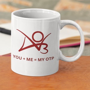 K&ouml;nnte beinhalten: Wei&szlig;e Keramiktasse mit einer roten Grafik einer stilisierten Person mit dem Text "YOU + ME = MY OTP" auf der Vorderseite.