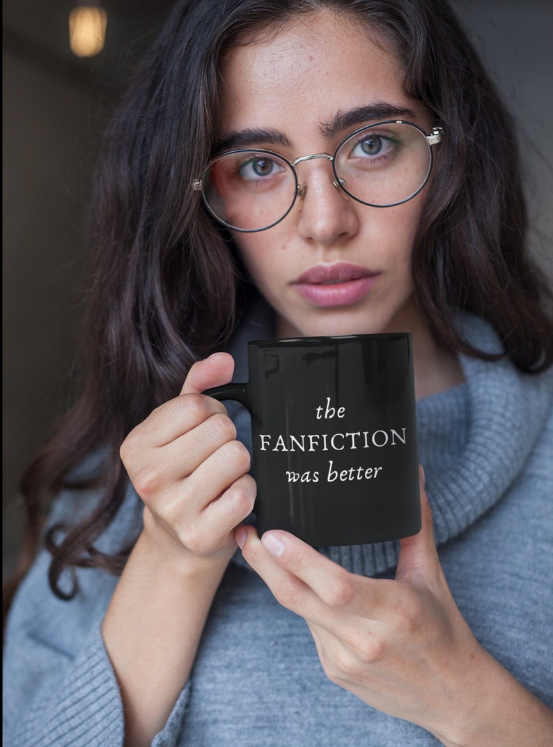 May include: A black coffee mug with white text that reads "the FANFICTION was better".