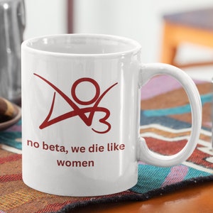 K&ouml;nnte beinhalten: Wei&szlig;e Keramiktasse mit einer roten Grafik einer Person mit dem Text "no beta, we die like women".