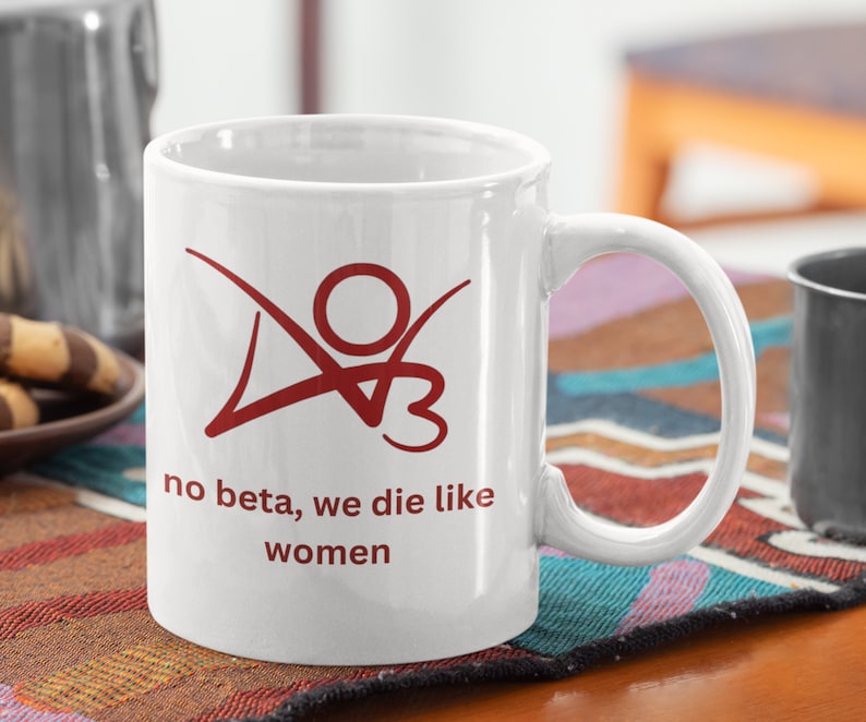 K&ouml;nnte beinhalten: Wei&szlig;e Keramiktasse mit einer roten Grafik einer Person mit dem Text "no beta, we die like women".