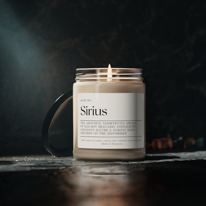 Puede incluir: Una vela beige en un tarro de vidrio con una tapa negra. La vela est&aacute; encendida y la etiqueta dice "smells like Sirius" y "THE AROUSING AMORTENTIA AROMA OF BAD BOY BRAVADO, ANIMALISTIC ANIMAGUS ALLURE & MAKING SOME MISCHIEF ON THE MOTORBIKE".