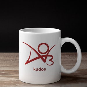 K&ouml;nnte beinhalten: Wei&szlig;e Keramiktasse mit einem roten Logo einer stilisierten Person mit dem Wort "kudos" darunter.