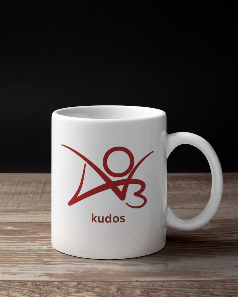 K&ouml;nnte beinhalten: Wei&szlig;e Keramiktasse mit einem roten Logo einer stilisierten Person mit dem Wort "kudos" darunter.