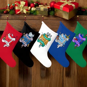 Puede incluir: Cinco calcetines navideños rojos, negros, blancos, azules y verdes cuelgan de una superficie de madera. Cada calcetín tiene un nombre y una clase de un juego de rol, como "Paladín" y "Bárbaro", con un gráfico de dados.