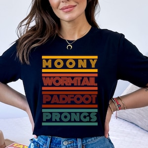 May include: Black t-shirt with a retro-style graphic design featuring the words "Moony", "Wormtail", "Padfoot", and "Prongs" in colorful stripes.