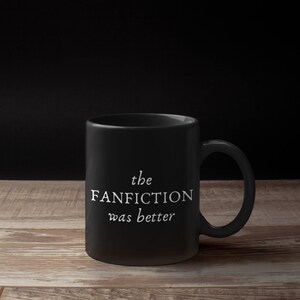 May include: Black ceramic coffee mug with white text that reads "the FANFICTION was better".