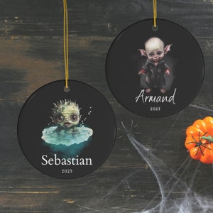 Pu&ograve; includere: Due ornamenti rotondi in ceramica nera con cordini dorati. Uno presenta una creatura verde nell'acqua con il nome "Sebastian" e "2023". L'altro mostra una creatura con una giacca nera con il nome "Armand" e "2023".