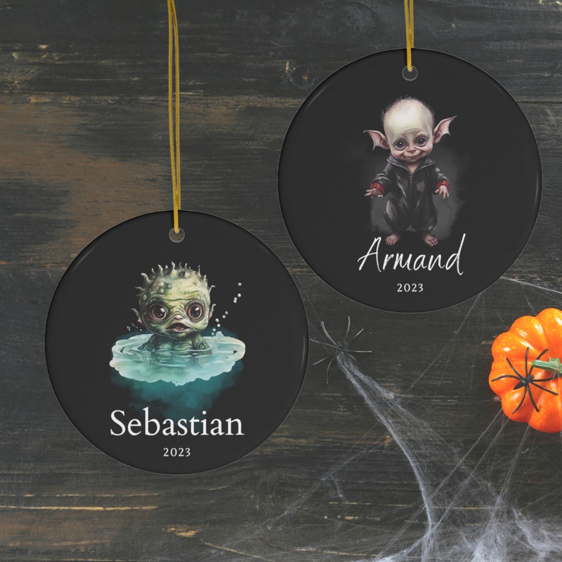 Pu&ograve; includere: Due ornamenti rotondi in ceramica nera con cordini dorati. Uno presenta una creatura verde nell'acqua con il nome "Sebastian" e "2023". L'altro mostra una creatura con una giacca nera con il nome "Armand" e "2023".