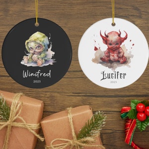Pu&ograve; includere: Due ornamenti natalizi rotondi in ceramica. Uno &egrave; nero con un'illustrazione di mostro verde e grigio e il nome "Winifred" e l'anno "2023". L'altro &egrave; bianco con un'illustrazione di diavolo rosso e il nome "Lucifer" e l'anno "2023".