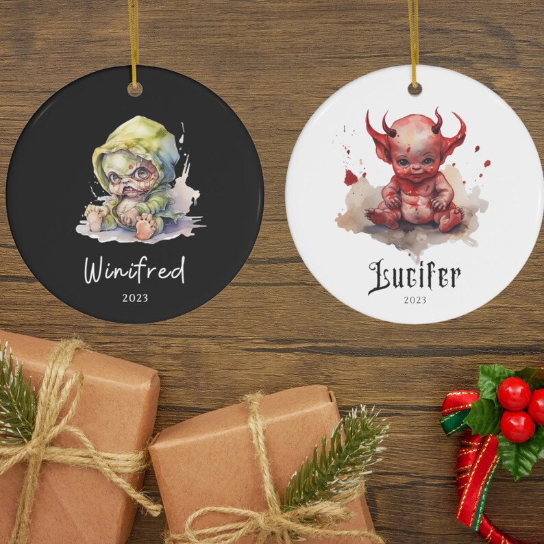 Pu&ograve; includere: Due ornamenti natalizi rotondi in ceramica. Uno &egrave; nero con un'illustrazione di mostro verde e grigio e il nome "Winifred" e l'anno "2023". L'altro &egrave; bianco con un'illustrazione di diavolo rosso e il nome "Lucifer" e l'anno "2023".