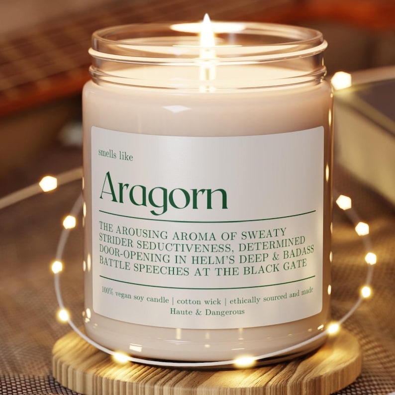 Puede incluir: Un tarro de vela de vidrio transparente con una vela beige en su interior. La etiqueta dice "smells like Aragorn" y describe el aroma como "El aroma estimulante de la seductora sudoraci&oacute;n de Strider, la determinaci&oacute;n de abrir puertas en la profundidad de Helm y los discursos de batalla badass en la Puerta Negra." La etiqueta tambi&eacute;n indica que la vela es 100% vela de soja vegana, mecha de algod&oacute;n, de origen &eacute;tico y hecha por Haute & Dangerous.