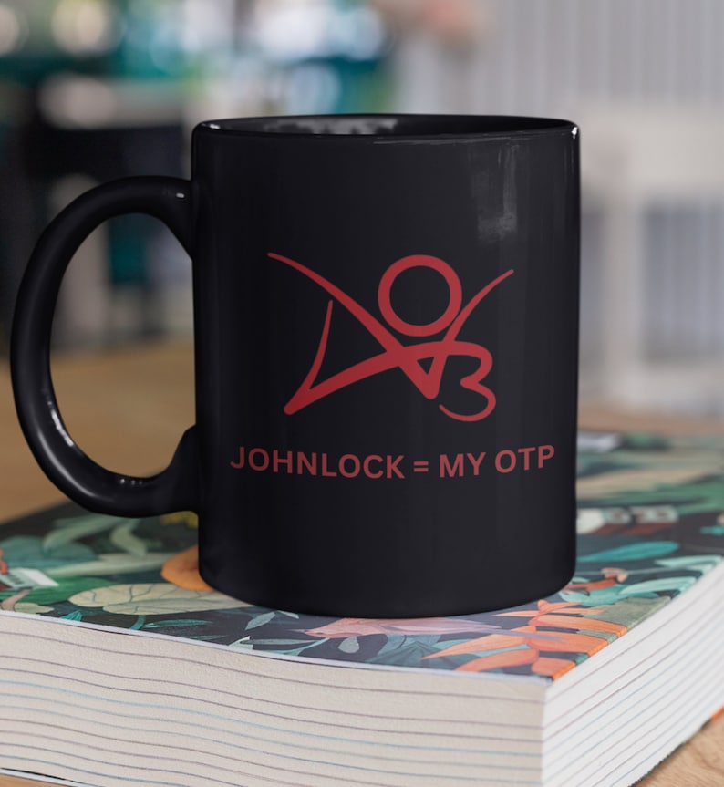 K&ouml;nnte beinhalten: Schwarze Keramik-Kaffeetasse mit einer roten Grafik einer Person mit dem Text "JOHNLOCK = MY OTP" auf der Vorderseite.