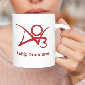 K&ouml;nnte beinhalten: Eine wei&szlig;e Keramiktasse mit einer roten Grafik einer Strichm&auml;nnchenfigur mit dem Text "I ship Dramione".