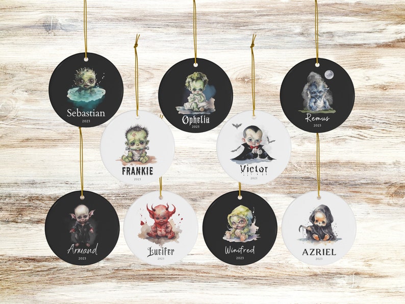 Pu&ograve; includere: Una collezione di ornamenti rotondi in ceramica con cordini dorati. Ogni ornamento presenta un'illustrazione ad acquerello di un personaggio di bambino spettrale, con nomi come "Sebastian", "Frankie" e "Victor" stampati sotto l'immagine, insieme all'anno 2023 o 2021.