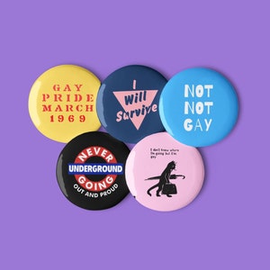 Könnte beinhalten: Fünf runde Knöpfe mit verschiedenen Botschaften und Designs. Die Knöpfe sind blau, rosa, gelb und schwarz. Die Botschaften auf den Knöpfen lauten "Gay Pride March 1969", "Will Survive", "Not Not Gay", "Never Going Underground Out and Proud" und "I don't know where I'm going but I'm gay".